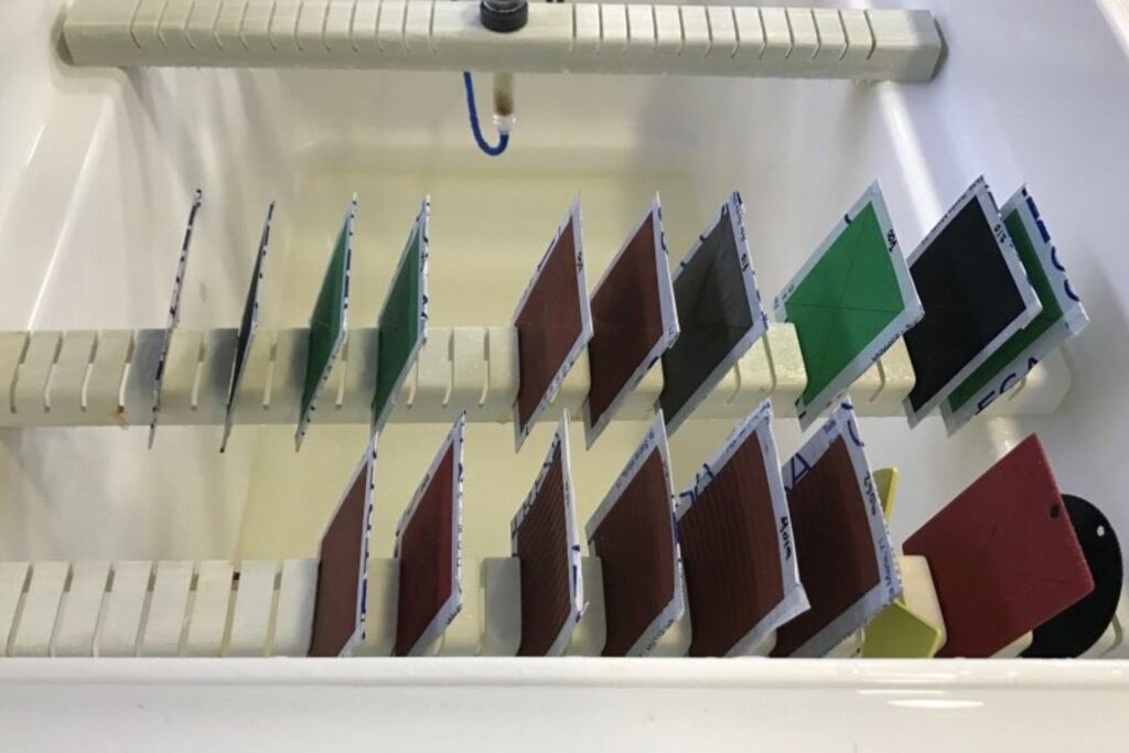 Muestras metálicas colocadas dentro de una cámara de niebla salina para ensayo de resistencia a la corrosión en laboratorio.