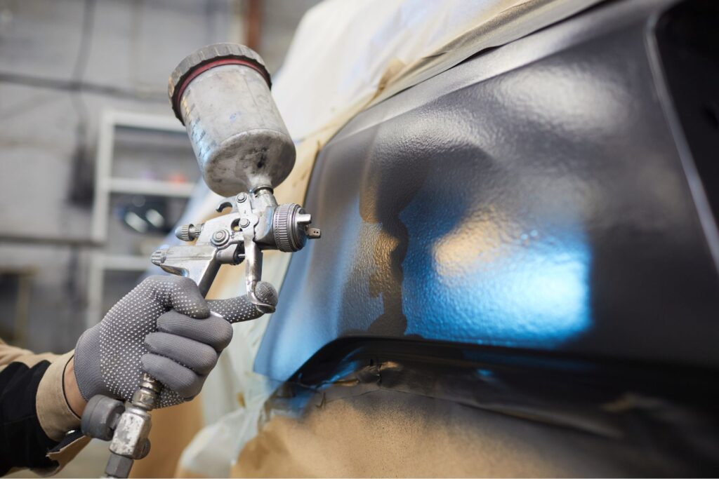 Una pistola de pintura echando pintura sustentable en una pieza industrial